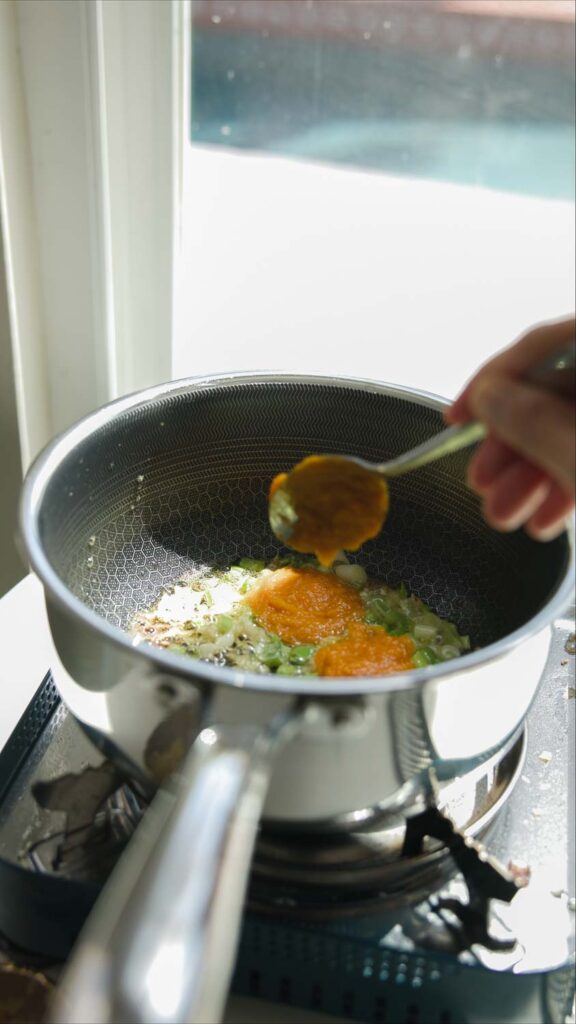 adding pumpkin puree to pot of broth